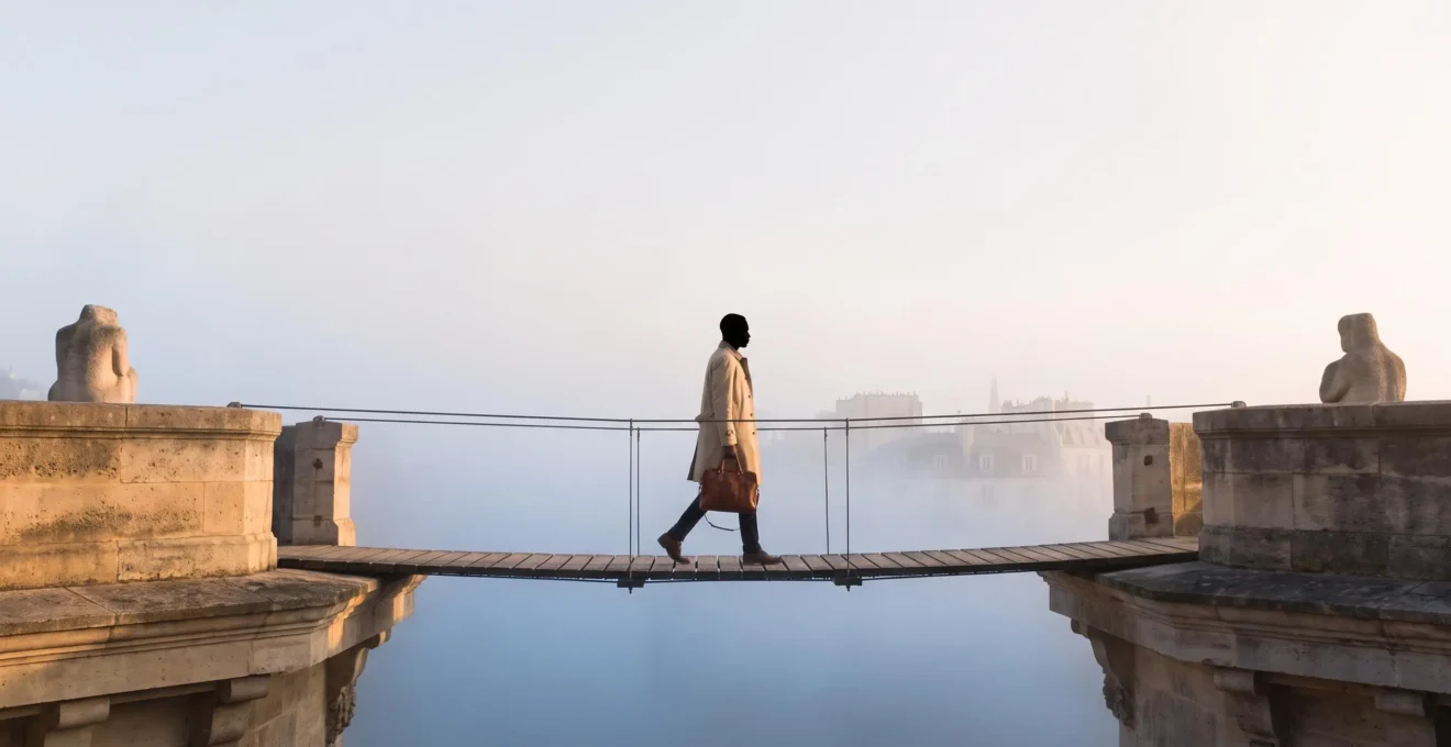 Illustration symbolique d'un salarié franchissant un pont suspendu au-dessus d'un vide, représentant la transition de couverture santé entre deux emplois