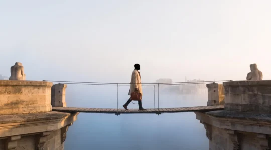 Illustration symbolique d'un salarié franchissant un pont suspendu au-dessus d'un vide, représentant la transition de couverture santé entre deux emplois